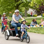 Families enjoying a sunny day cycling on tricycles in a vibrant park.
